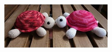 Zwei gehäkelte Amigurumi-Schildkröten mit rot- und pink-melierten Panzern auf Holz.
