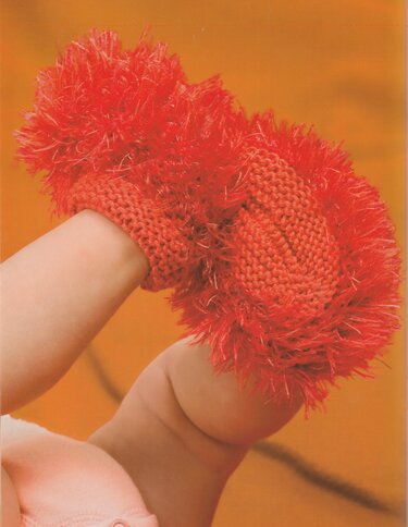 Nahaufnahme eines Babyfußes mit einem roten, flauschigen gestrickten Babyschuh mit Fransen.