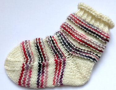 Gestrickte Babysocke in Creme mit farbigen Streifen und Rippenbündchen.