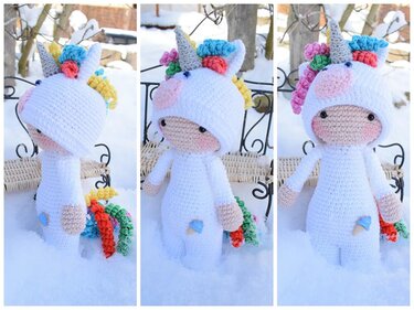 Gehäkelte Amigurumi-Einhornpuppe im weißen Kostüm mit bunter Mähne und Schweif im Schnee.