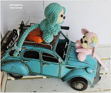 Zwei gehäkelte Amigurumi-Affen, türkis und rosa, sitzen auf einem türkisfarbenen Retro-Spielzeugauto