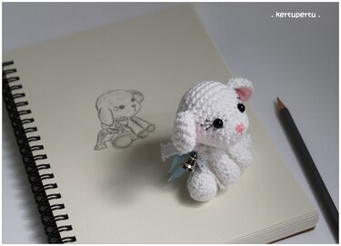 Weißes gehäkeltes Amigurumi-Hündchen mit Glocke auf Skizzenblock