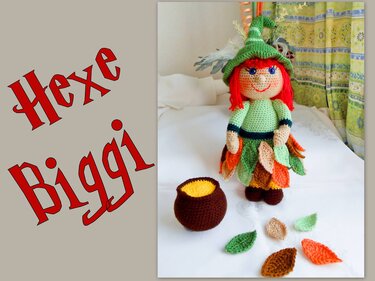 Gehäkelte Hexe mit rotem Haar, grüner Mütze und Blätterrock neben braunem Kessel und losen Blättern