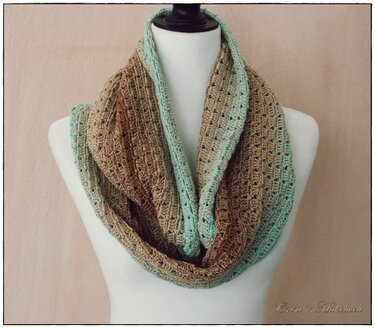 Gehäkelter Loop-Schal mit Türkis-Braunem Farbverlauf auf Schneiderpuppe, offenes Maschenmuster.