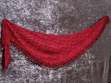 Rotes gestricktes Dreieckstuch mit Ajourmuster und Fransen auf dunklem Hintergrund