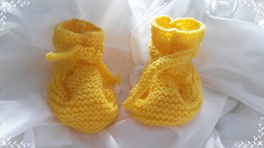 Gelbe gestrickte Babyschuhe mit Bindeband auf weißem Stoff