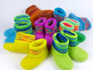 Mehrere bunte, gestrickfilzte Hausschuhe mit gerippten Bündchen auf weißem Hintergrund.