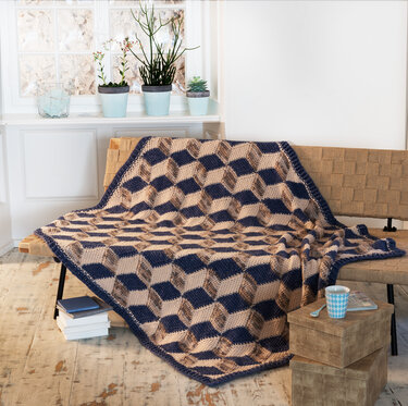 Gehäkelte Decke mit blau-beigem 3D-Würfelmuster auf einer Bank