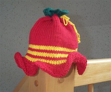 rote gestrickte Kinder‑Mütze mit gelben Streifen und grünem Zipfel