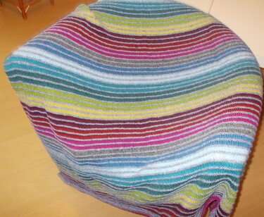 Bunte, gestreifte Strickdecke über einem Möbelstück auf hellem Holzboden.