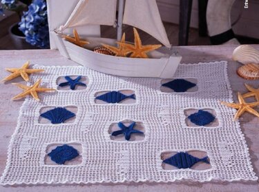 Rechteckiges weißes Häkeldeckchen mit neun blauen maritimen Motiven (Seesterne, Fische, Muscheln) in quadratischen Aussparungen.