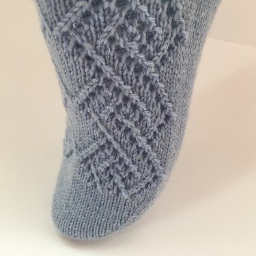 Nahaufnahme einer hellblauen gestrickten Damensocke mit Rauten-Lochmuster auf dem Spann
