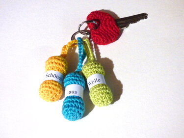 Amigurumi‑Schlüsselanhänger mit drei gehäkelten Wollknäueln (Gelb, Türkis, Lindgrün) und rotem Häkelherz