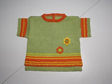 Grünes kurzärmeliges Strickshirt für Babys mit orange-gelben Streifen am Saum und zwei aufgenähten Blumen-Applikationen.