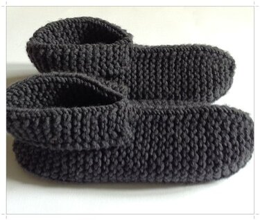 Ein Paar dunkelgraue, handgestrickte Hausschuhe aus Garn, nebeneinander auf hellem Untergrund.