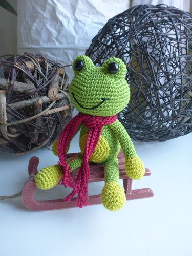 Häkel-Amigurumi: grüner Frosch mit rotem Schal auf kleinem Holzschlitten, Detailansicht
