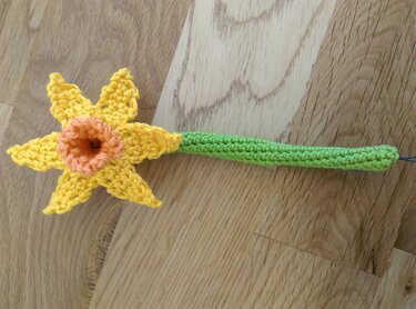 Gehäkelte gelbe Narzisse mit orangefarbener Trompete und grünem Stiel auf Holzuntergrund