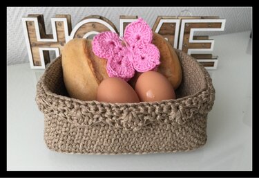 Gehäkelter Korb mit Brötchen, Eiern und rosa Schmetterling