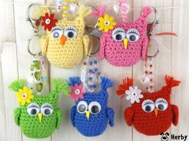 Fünf farbige Amigurumi‑Eulen‑Anhänger mit Wackelaugen, Blumenapplikationen und Perlenketten