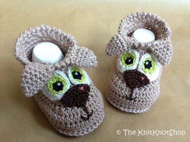 Beige gehäkelte Babyschuhe mit Hunde-Gesicht, grünen Augen und Schlappohren