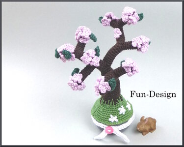 Gehäkelter Kirschblütenbaum mit rosa Blüten und grünen Blättern in grünem Topf; daneben eine kleine braune Hasenfigur.