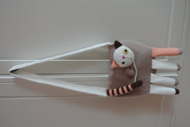 Gehäkelte Katzen-Umhängetasche in Beige mit langem weißen Trageriemen und hängenden Beinen