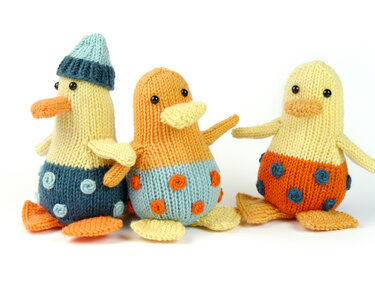 Three knitted amigurumi ducklings with polka-dot bellies on a white background