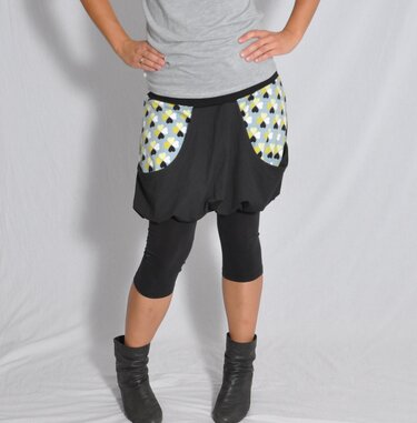 Kurzer schwarzer Ballonrock mit großen aufgesetzten Taschen im Herzmuster, kombiniert mit schwarzen 3/4-Leggings und Stiefeletten