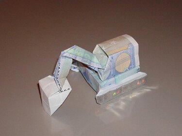 Gefalteter Origami-Bagger aus Euro-Banknoten auf neutralem Untergrund.