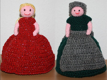 Zwei gehäkelte Amigurumi-Puppen, links rotes glänzendes Kleid, rechts grünes Oberteil mit grauer Schürze