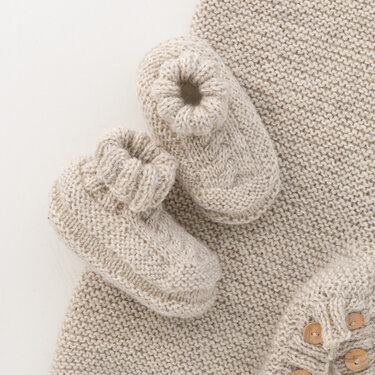 Gestrickte Babyschuhe mit Umschlagbündchen auf krausrechts gestrickter Decke, Knöpfe am Rand sichtbar