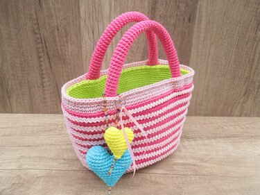 Gehäkelte rosa-weiße Henkeltasche mit grüner Innenseite und zwei Herzanhängern