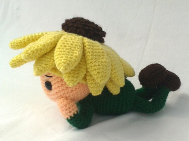 Gehäkelte Amigurumi-Blumenpuppe mit gelben Blütenblättern, grünem Körper und braunen Details, seitliche Ansicht