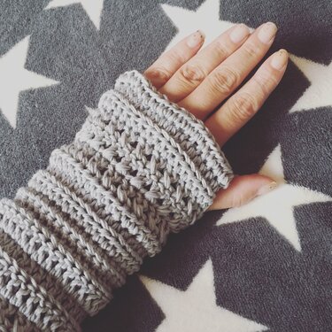 Hand mit grauer gehäkelter Armstulpe auf Decke mit Sternenmuster