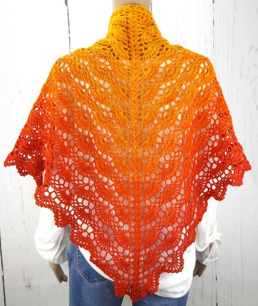 Back of a crochet triangle shawl with an orange-to-red gradient and scalloped edge, draped on a display mannequin wearing a white shirt and jeans.