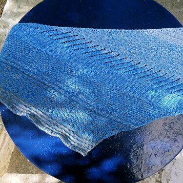 Gestricktes blaues Dreieckstuch mit diagonalen Lochreihen auf dunklem runden Untergrund