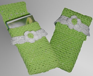 Zwei gehäkelte Utensilos in Limettengrün mit weißer Blumenapplikation; eines enthält ein Buch.