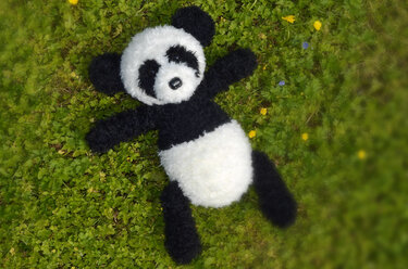 Gehäkelter schwarz-weißer Panda liegt auf grüner Wiese mit kleinen Blumen