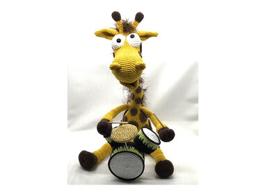 Gelbe gehäkelte Amigurumi-Giraffe mit braunen Flecken, die auf einem weißen Hintergrund sitzt und drei kleine Trommeln hält.