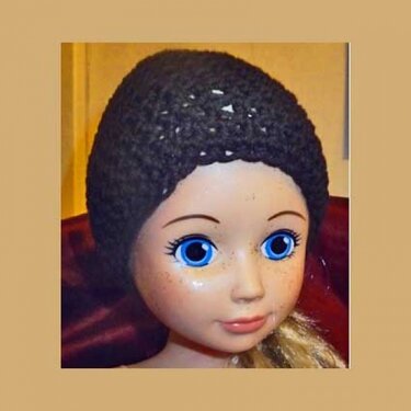 Frontansicht einer Puppe mit dunkelgrauer, gehäkelter Mütze und blondem Haar.