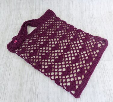 Dunkellila gehäkelte Henkeltasche mit Herzmuster auf hellem Holzuntergrund.