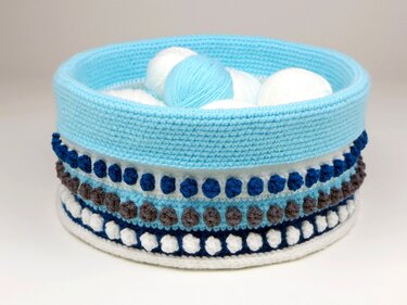 Runder gehäkelter Utensilo-Korb mit Noppenmuster in Blau, Weiß und Braun, gefüllt mit Garnknäueln