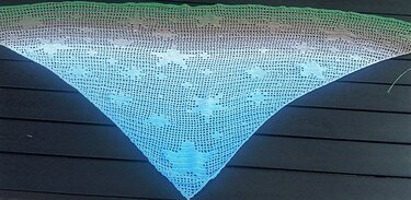Gehäkeltes dreieckiges Tuch mit Sternmotiven und grün-blauem Farbverlauf auf dunklem Holz