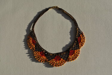 Dunkelbraune Spitzenkette mit orange-goldenen Fächern und Metallverschluss auf hellem Hintergrund