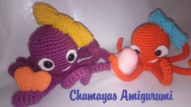 Zwei gehäkelte Amigurumi-Oktopusse, einer lila mit gelbem Kopfband, einer orange mit blauem Kopfband, beide mit großen Augen und kleinen Applikationen