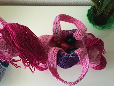 Häkelanleitung Einhorn-Henkeltasche in Rosa und Lila, mit verpackten Süßigkeiten im Inneren.