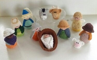 Gehäkelte Mini-Krippenfiguren mit Krippenbaby, Engeln, Hirten und Tieren auf hellem Untergrund
