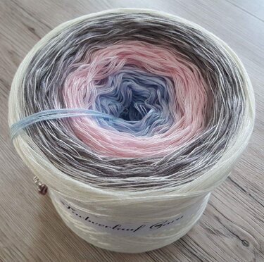 Garnknäuel mit Farbverlauf in Weiß, Grau, Rosa und Hellblau auf Holzboden.