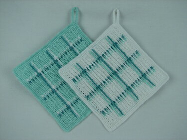 Zwei gehäkelte, quadratische Topflappen in Türkis und Weiß mit Karomuster und Aufhängeschlaufen.