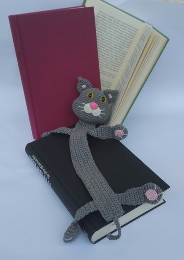 Gehäkeltes graues Katzen-Lesezeichen mit rosa Nase und Pfoten, auf Büchern platziert
